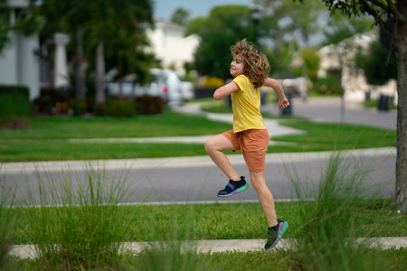 Cute kid boy running across american neighborhood street. Summer, childhood, leisure and people concept. Happy little blonde child boy running in summer park outdoor. Sport and run.の写真素材