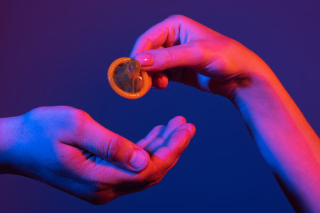 Hand with condom. Passion, pleasure, desire game, prelude, couple hand holds condom. Closeup of couple giving condom. Condom in male hand and female hand. Give condom safe sex concept.の写真素材