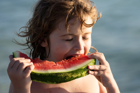 Child with watermelon on summer beach outdoor. Kid having fun in summer day. Kids summer vacation and healthy eating. Kittle kid eats juicy watermelon on the beach, coast, seashore. Summer fruits.の写真素材