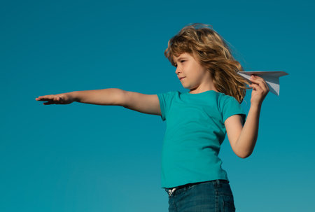 Child boy with paper plane against blue sky. Child dreaming, throwing paper plane, toy airplane. Imagination, kids freedom.の写真素材