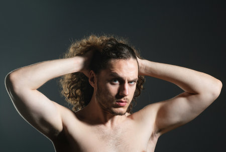 Man with curly hair. Healthy curly hair, close up portrait of attractive masculine handsome macho brutal guy with long curly isolated on gray background. Mans modern haircut.の写真素材