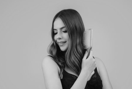 Smiling woman brushing hair with comb. Beautiful girl combing long hair with hairbrush.の写真素材