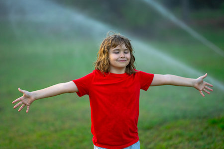 Kids play with water hose, sprinkler watering grass in the garden. Summer garden outdoor fun for children. Boy splashing water on hot summer day. Kid watering plants and grass in backyard.の写真素材