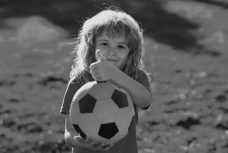 Kid playing soccer, happy child enjoying sports football game, kids activities, little soccer player. Active sporty kid soccer show thumbs up success sign.の写真素材