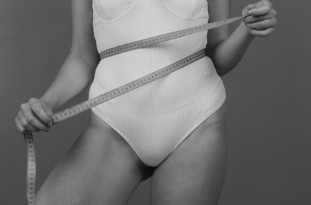 Slim girl holding a centimeter around the waist line. Slim young woman measuring her waist with a...