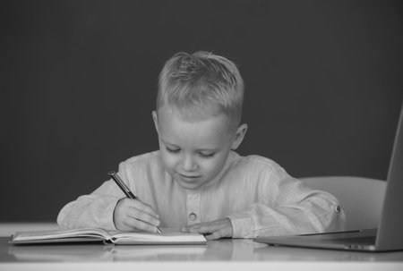 Portrait of funny pupil of primary school study in classroom at school. Kid writing in notebook in class. Education and kids knowledge concept.の写真素材