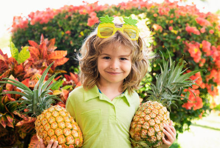 Young funny boy holding pineapple and smiling in backyard. Kid with pineapple. Kids summer fruit.の写真素材