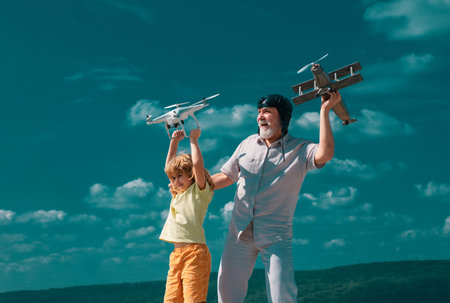 Old grandfather and young child grandson with plane and quadcopter drone over blue sky and clouds background.の写真素材