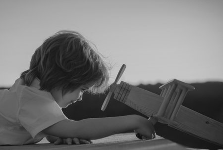 Happy kid playing with toy airplane against blue sky background. Cute child walking on a sunny summer day. Kids dreams of traveling.の写真素材
