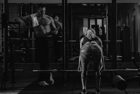 Couple training with barbell in gym. Muscular trainer man training woman with barbell.の写真素材