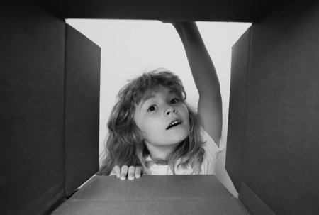 Cheerful cute child opening a present. Cardboard boxes, parcels. Delivery service concept. Kid opening package.の写真素材