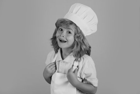 Kid chef funny face. Child chef dressed cook baker apron and chef hat isolated on studio background. Healthy nutrition kids food.の写真素材