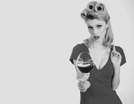 Woman with glass of red wine. Beautiful woman drinking red wine, isolated on white. Retro girl with stylish makeup and retro hairstyle in white dress tasting red wine.の写真素材