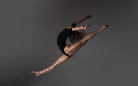 Leg-split jump. Flexible sexy body of young woman on black background. Sexy woman exercise. Fit slim sexy woman body in bodysuit. Sexy woman stretching pose stretch. Fit fitness athlete stretches.の写真素材