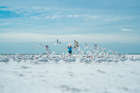 Happy amazed kid running, chasing birds. Child and seagull on the beach. Amazed boy running on the beach with his hands raised up with flying seagulls birds.の写真素材