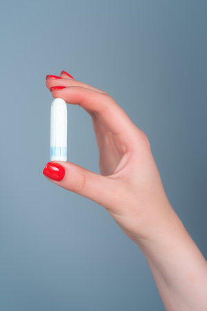 Hand holding menstruation tampon. Womens menstrual cramps. Feminine tampon. Hygienic tampon in female hand close-up. Critical days, menstrual period. Gynecological health care. Cotton tampon.の写真素材