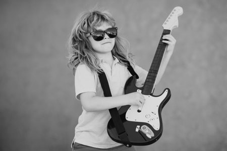 Portrait of a funny child with glasses practicing a song during a guitar lesson on street. Music...