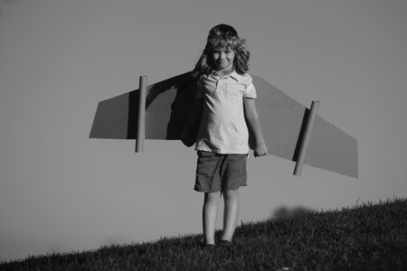 Portrait of cute blond child play pilot with handmade craft paper plane wings. Kids dreaming, success, creative and startup concept.の写真素材