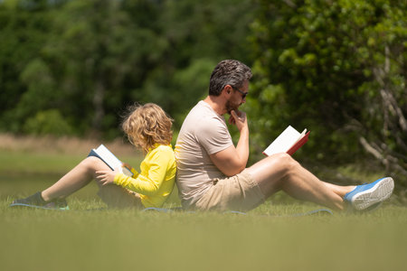 Outdoor school. Father and son reading book in park, man encourages boy to knowledge, family education. Father and child read bookin park. Parent reading with child book on summer nature in park.の写真素材