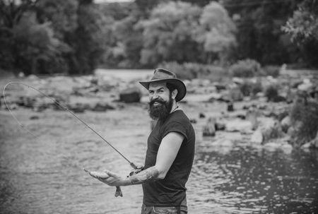 Hipster bearded man catching trout fish. Fisherman caught a fish. Man fishing on river.の写真素材
