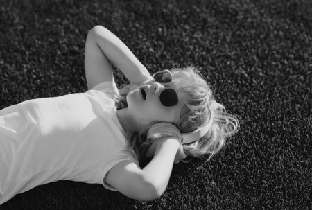 Kid listening to music in headphones. Cute child in summer sunglasses enjoying music outdoor.の写真素材