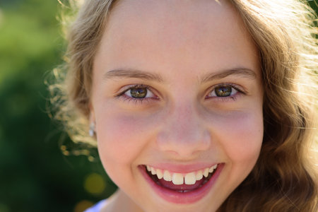 Cute little smiling happy girl close up face. Outdoor closeup portrait of funny kids face. Summer kid outdoor portrait. Close up face of cute child. Kid having fun outdoor on summer day.の写真素材