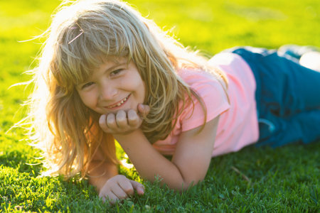Summer child face. Smiling child boy with grass background. Happy childhood. Boy lying on grass. Cute kid child enjoying summer on field. Dreaming kids concept.の写真素材