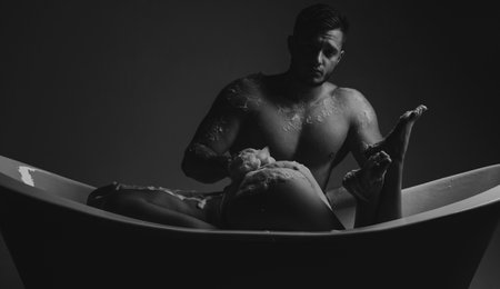 Couple in bathroom. Prelude couple in love. Girl washing in bath with foam. Sex games and orgasm. Spa and relaxation. Isolated on dark. Love relations of couple in bath with foam. Love and trust.の写真素材