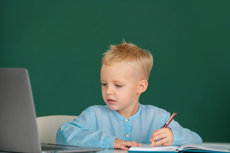 Funny face of little student of primary school study in classroom at school. Kid writing in notebook...
