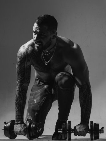 Muscular guy doing exercises with dumbbell. Sporty man working out. Muscular torso on gray background. Strength and motivation. Strong bodybuilder with six pack, perfect abs, shoulders, biceps chest.の写真素材