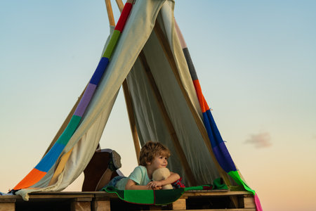Camp dream. Kid dreams in tent outdoor. Childhood dream. Daydreamer child. Dreams and imagination. Dreamy kids. Child sitting in tent at summer camp. Cute kid spend summer holidays in countryside.の写真素材