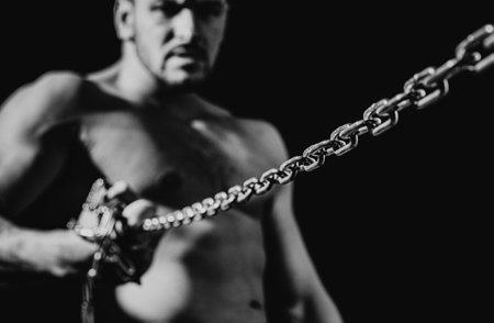 Muscular guy with chains on shoulders against a black background.の写真素材