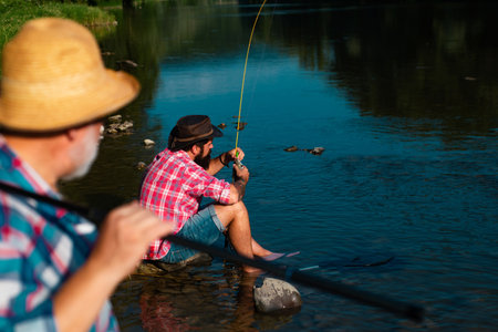 Young and old fisherman standing on the shore of lake with fishing rod. Father and son enjoy life....