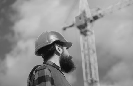 Male construction worker in work clothes and a construction helmet. Improvement and renovation. Brutal man builder. Engineer builder in uniform. Construction crane.の写真素材