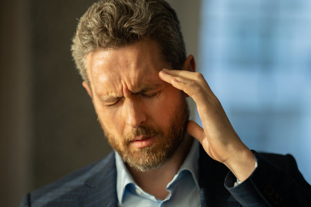 Man with sinus headache, tension or cluster headache, close up portrait. Head pain concept. Cephalalgia and migraine. Migraine symptoms. Chronic headaches. Headache triggers.の写真素材