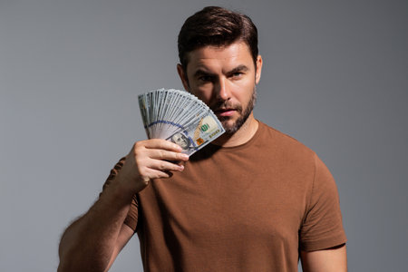 Man showing cash money in dollar banknotes. Portrait of business man isolated on gray studio...