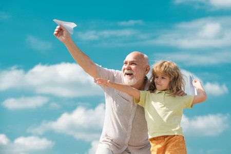 Grandfather and son playing with paper plane against summer sky background. Child boy with dreams of flying or traveling.の写真素材