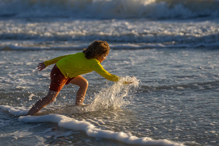 Happy child playing in splashing water on summer sea. Summer vacation. Kid play of waves at sea. little kid playing in sea and splashes water drops. Child play splash water on sea. Summer vacation.の写真素材