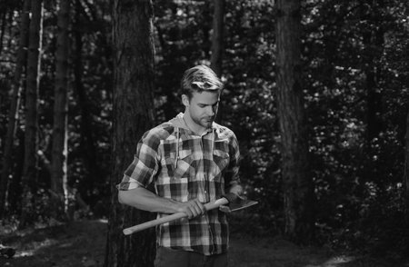 Lumberjack standing with axe on forest background. Deforestation is a major cause of land degradation and destabilization of natural ecosystems.の写真素材