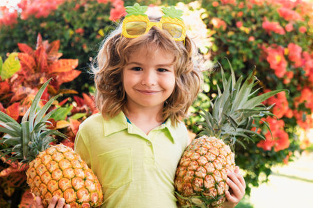 Little blonde kid hugging pineapple on nature background. Childhood, healthy nutrition, advertising. Close up kids funny face, copy space.の写真素材