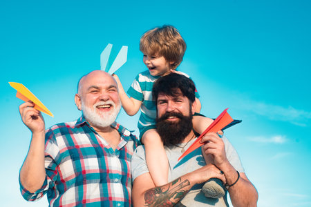 Child pilot aviator with paper airplane dreams of traveling. Fathers day - grandfather, father and son are hugging and having fun together.の写真素材