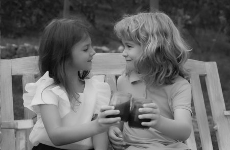 Two children drink smoothie, kids summer cocktail outdoors. Portrait of adorable brother and sister smile and laugh together while sitting on swing outdoors. Happy lifestyle kids.の写真素材