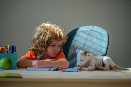 Cute little boy with puppy dog doing her homework. Education childhood and school concept - cute little student with pet writing to notebook at home.の写真素材