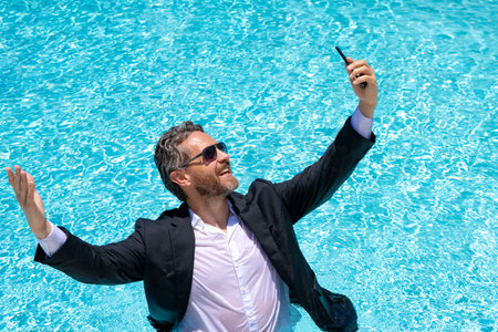 Hot business. Funny excited office worker with phone. Business man in suit used phone in beach. Travel and business. Crazy excited office worker taking a selfie at the beach. Businessman on summer.の写真素材