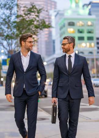 Businessmen communicating at meeting. Two businessmen discussing outdoor during business meeting. Businessmen talking. Business partners walking outdoor. 40s businessman walking by street.の写真素材