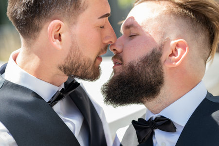 GGay kiss on wedding. Marriage gay couple tender kissing. Close up portrait of gay kissed together during wedding ceremony. Homosexual couple celebrating their wedding. LBGT couple at wedding ceremony.の写真素材