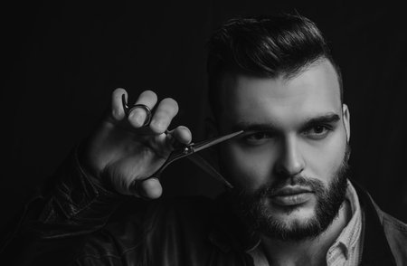 Young sexy man, portrait of guy with barber scissors for barber shop. Modern barbershop, shaving. Handsome male with modern hairstyle on black.の写真素材