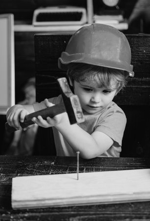 Child with helmet in orange hard hat. Tools construction. Boy hammering. Kid hammers nail.の写真素材