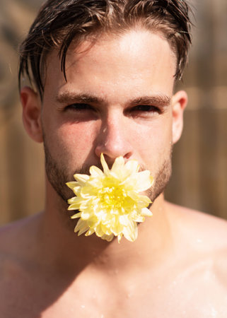 Man in love. Pride gay homosexual concept. Man face with flower in mouth, tongue. Handsome man close-up portrait.の写真素材