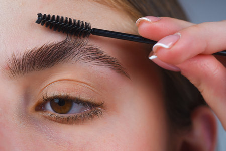 Perfect eyebrows. Close up of woman getting eyebrow make-up. Macro applying cosmetics on her eyebrow with brush. Perfect shape of eyebrow, brown eyeshadows and long eyelashes. Shape eyebrows.の写真素材